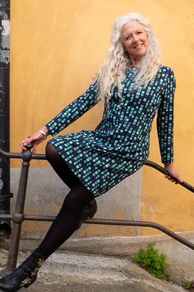 Grafisk klänning i blåa toner med båthals, lång ärm och längd till ovan knä från märket Esther & Inez