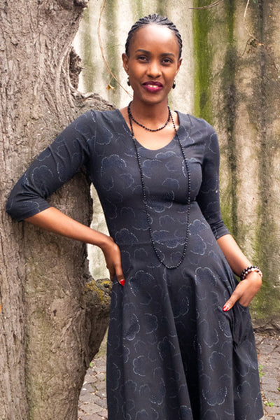 Klänningen Stina med klockad kjol, skärning i midjan, fickor, u-hals och trekvarts ärmar i tyg med fjärils mönster i svart och mörk brunt från märket Esther & Inez